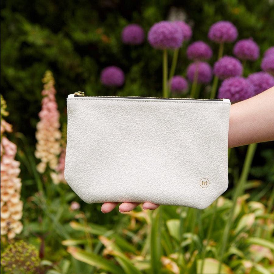 a woman in a garden holding a small white clutch handbag 